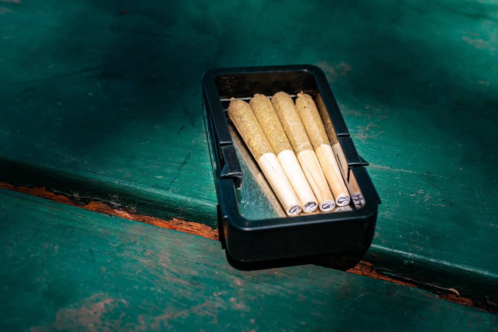 Pre-rolled cannabis joints in black tray on green wooden surface